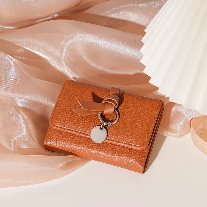 Celia pebbled vegan leather trifold wallet with knotted strap and silver-tone charm