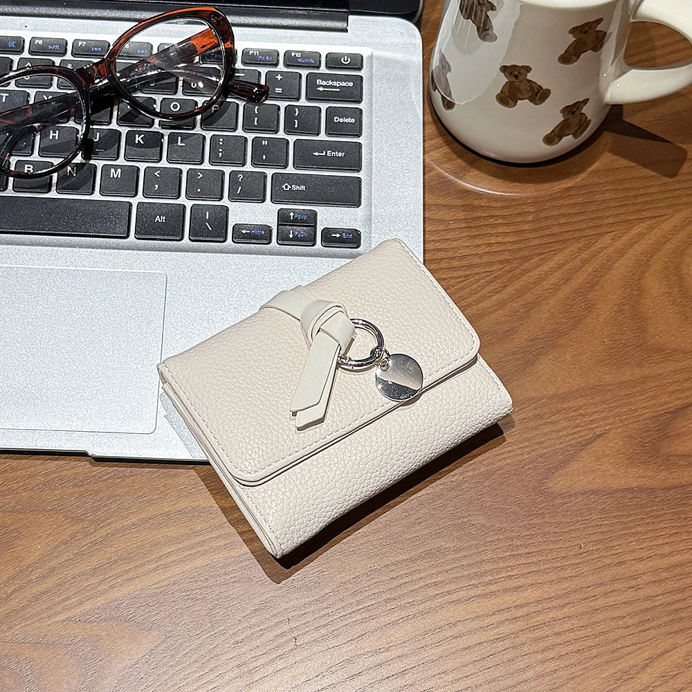 Celia pebbled vegan leather trifold wallet with knotted strap and silver-tone charm