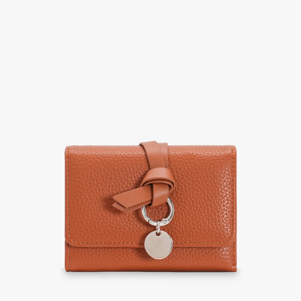 Celia pebbled vegan leather trifold wallet with knotted strap and silver-tone charm in Camel
