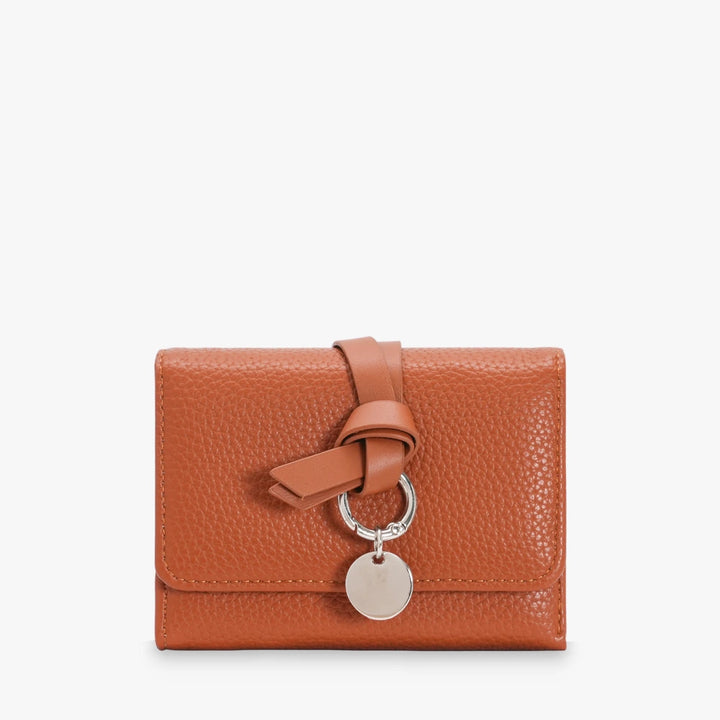 Celia pebbled vegan leather trifold wallet with knotted strap and silver-tone charm in Camel