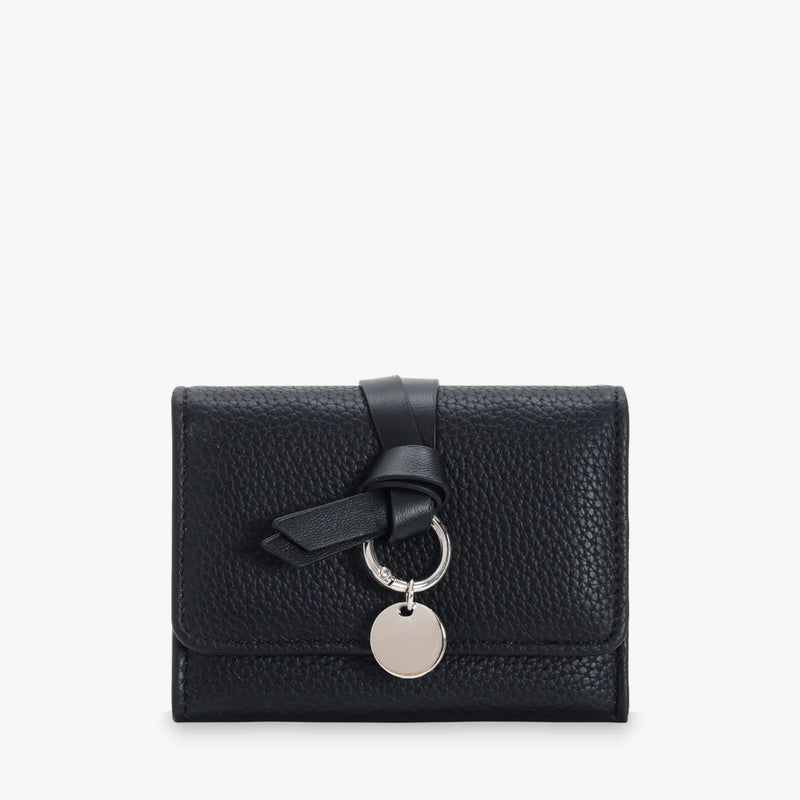 Celia pebbled vegan leather trifold wallet with knotted strap and silver-tone charm in Black